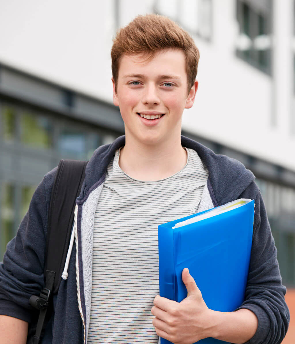 Young person holding a blue folder, wearing a striped shirt and a hoodie, with a backpack. Standing outdoors, smiling at the camera.